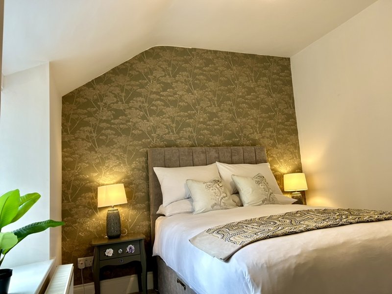 Bedroom with double bed, upholstered headboard, patterned accent wall, bedside lamps and side table