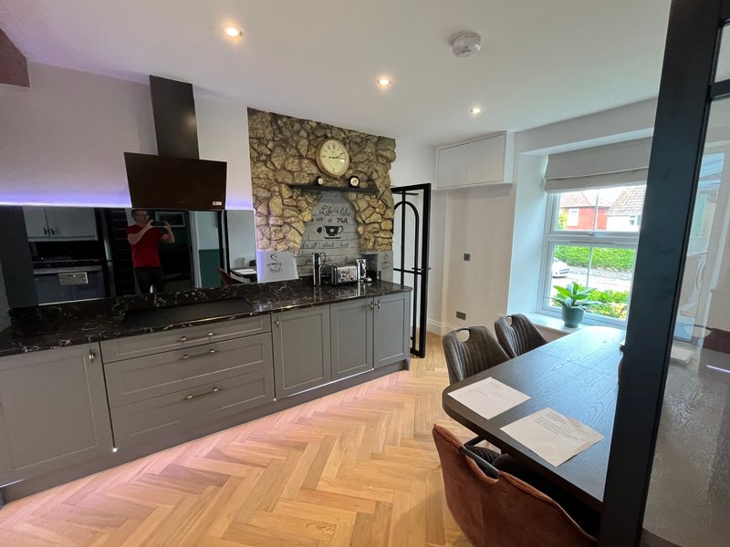 Modern kitchen and dining area with grey cabinetry, stone feature wall, wooden flooring and garden view