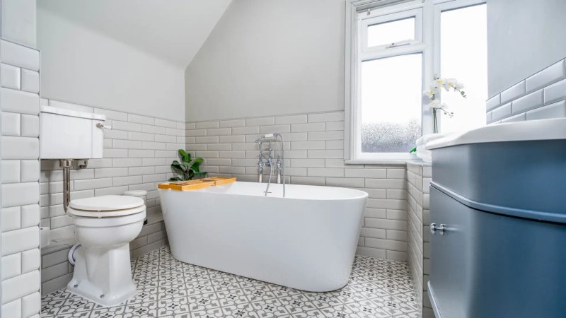 Modern bathroom with white subway tile walls, freestanding white bathtub, toilet, and window