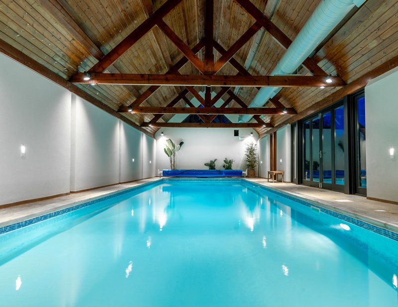Indoor swimming pool with wooden vaulted ceiling, white walls, and blue glass doors