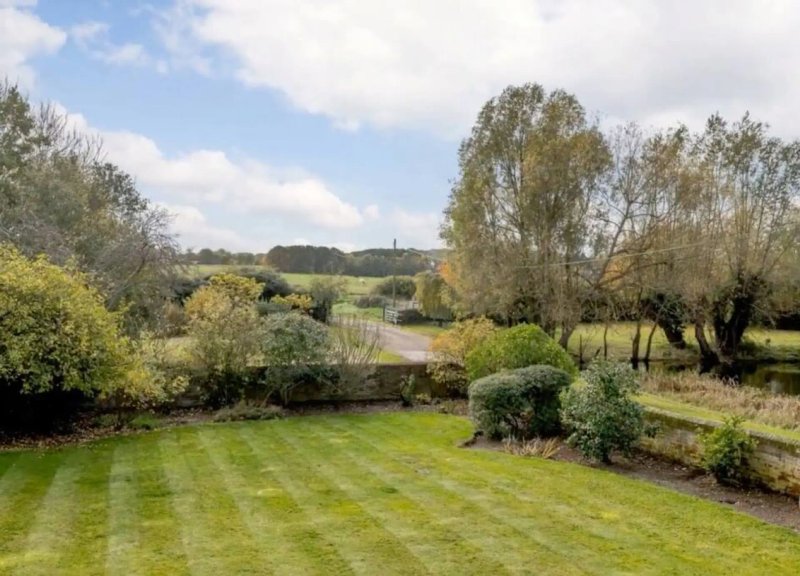 Large garden with mowed lawn, mature trees, and countryside views beyond