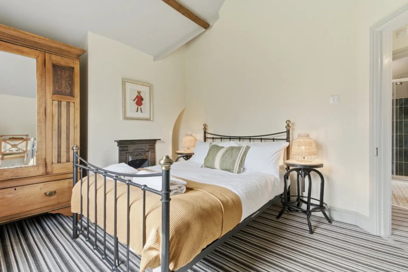 Bedroom with metal-frame bed, wooden wardrobe, fireplace, and striped floor