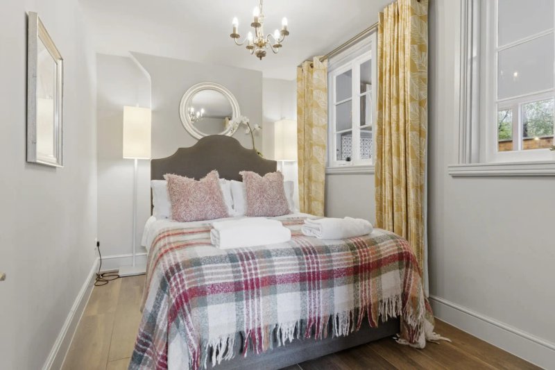 Bright bedroom with double bed, plaid throw blanket, gold curtains and pendant light