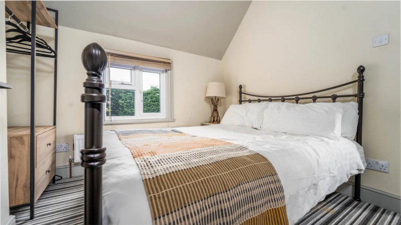 Bedroom with metal-frame bed, white bedding, patterned throw blanket, and striped carpet flooring