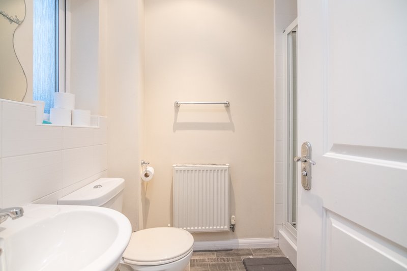 Clean bathroom with toilet, sink, radiator and shower enclosure