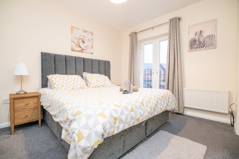 Bright bedroom with double bed, grey headboard, wooden nightstand and balcony access