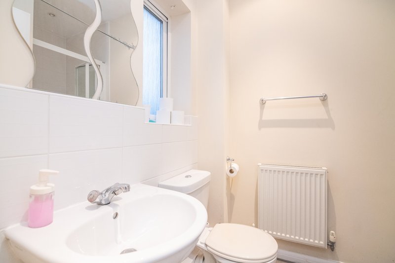 Clean modern bathroom with white sink, mirror, toilet, radiator and small window
