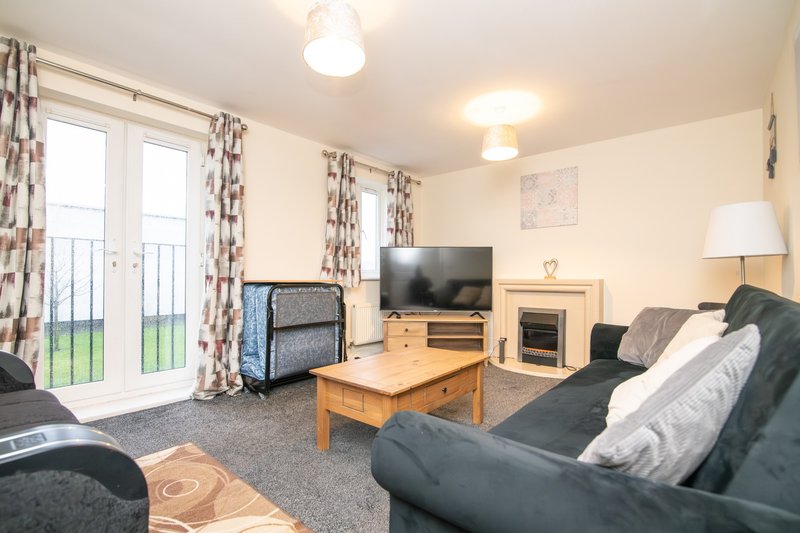 Living room with dark sofas, wooden coffee table, TV, fireplace and balcony doors