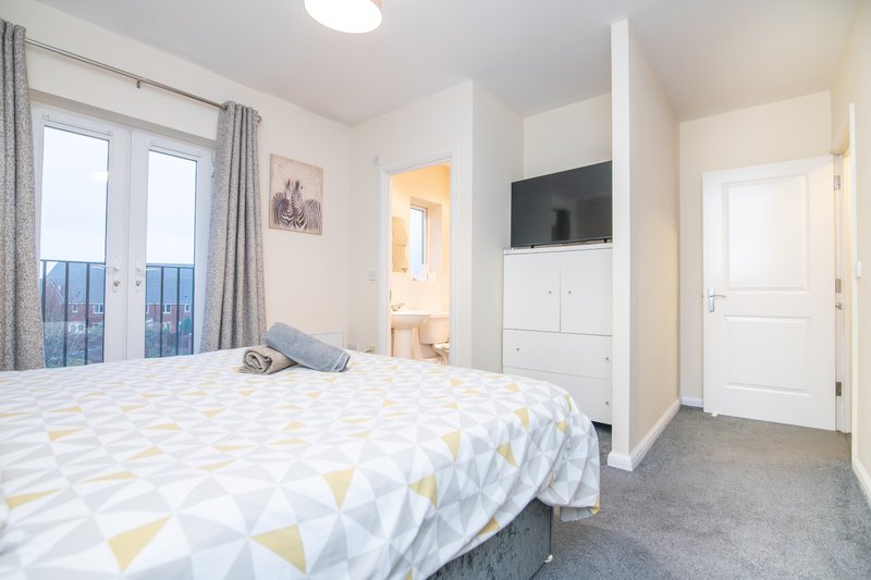 Bright bedroom with double bed, white storage unit, large windows with city views and grey curtains