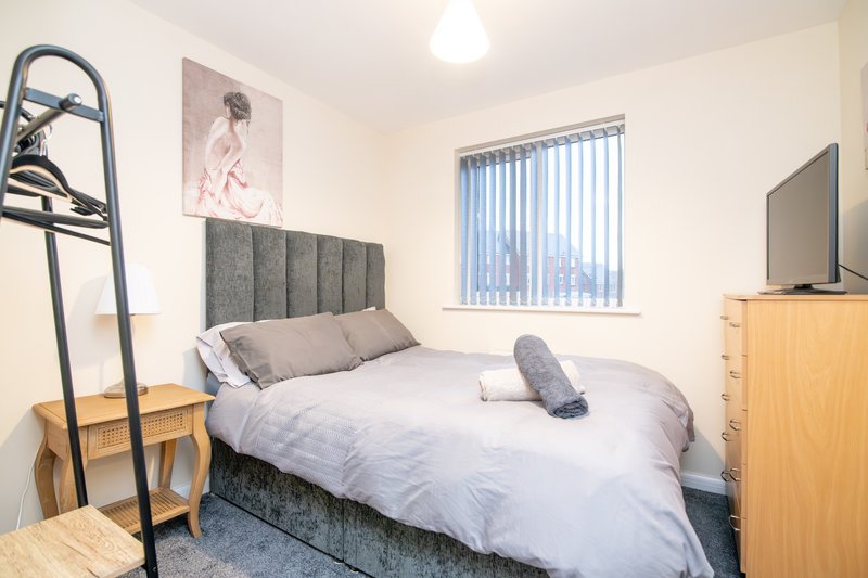 Bedroom with double bed, grey headboard, wooden furniture and vertical blinds window