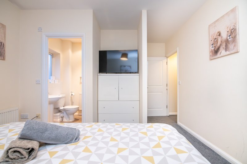 Bright modern bedroom with double bed, wall-mounted TV, ensuite bathroom, and geometric patterned bedding