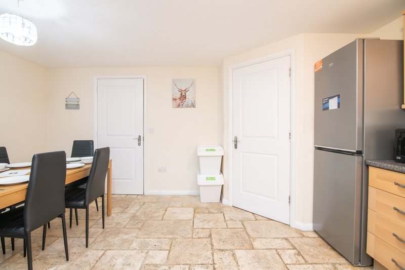 Open-plan kitchen and dining area with stainless steel fridge, wooden table, black chairs and stone flooring