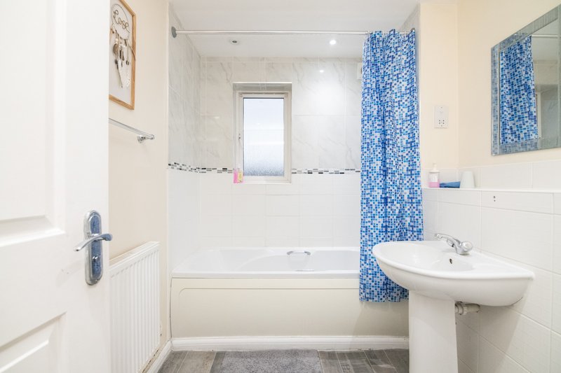 Clean bathroom with bathtub, pedestal sink, blue shower curtain and window