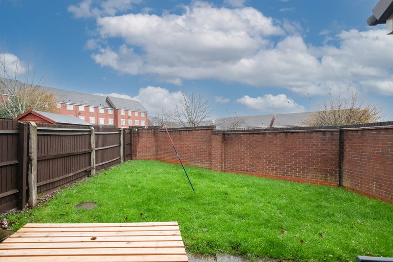 Enclosed brick-walled garden with green lawn, wooden decking, and metal gate