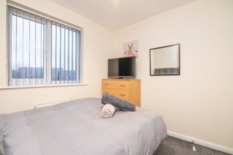 Bedroom with double bed, wooden dresser, television, mirror and vertical blinds