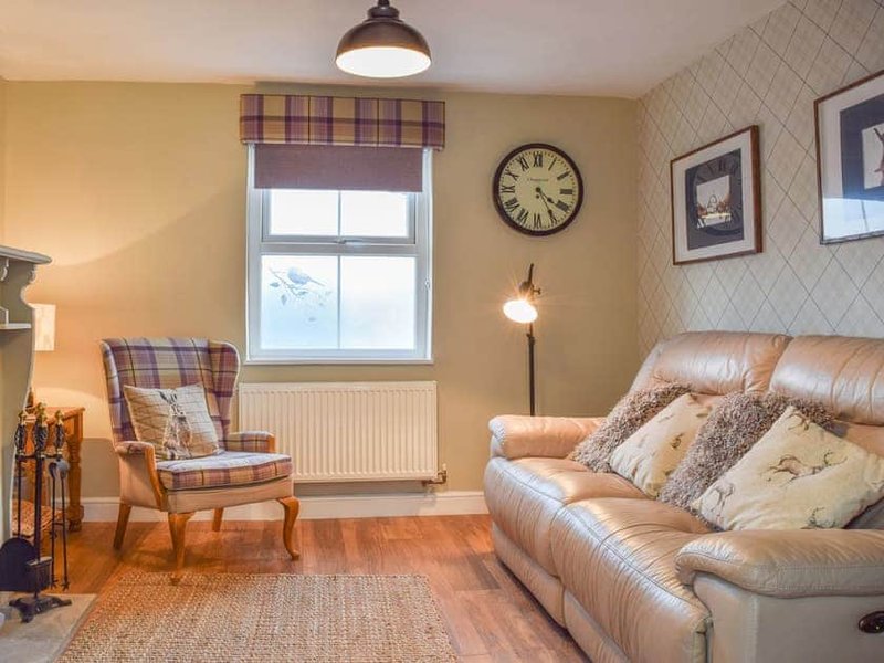 Warm living room with leather sofa, plaid armchair, wooden floor and window with tartan valance