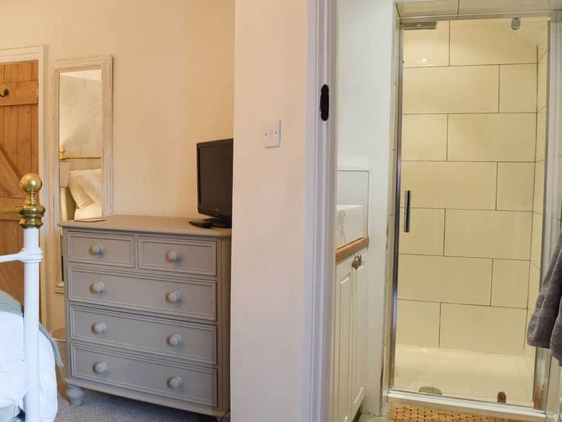 Bedroom with grey chest of drawers, monitor, and ensuite shower cubicle visible