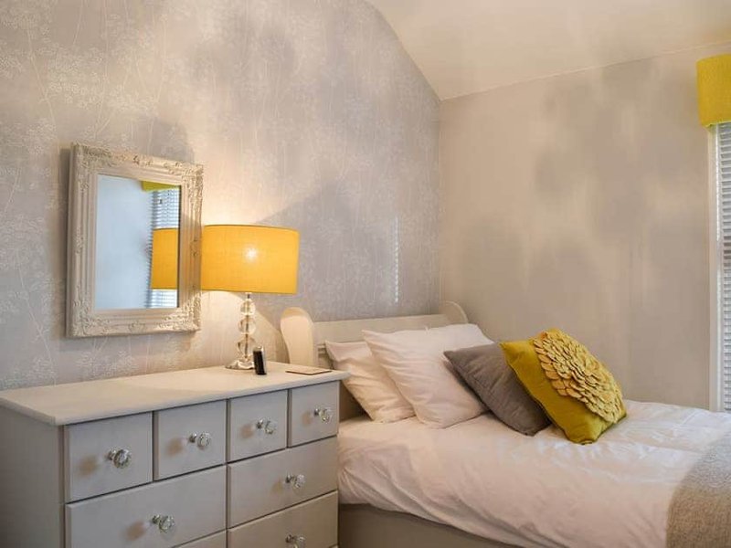 Bedroom with double bed, white dresser, yellow lamp and framed mirror on wall