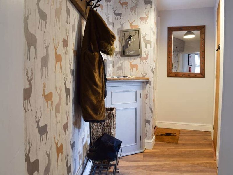 Hallway with deer-patterned wallpaper, wooden floor, coat hook with brown jacket and basket