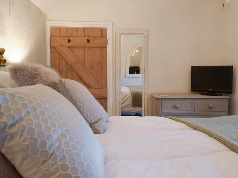Bedroom with white bedding, patterned cushions, wooden barn door headboard, mirror and TV.