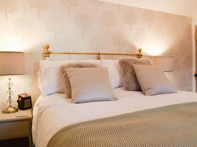 Bedroom with double bed, decorative pillows, brass headboard rail, bedside lamps and tree-patterned wallpaper