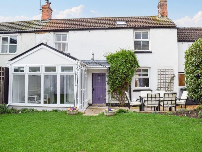 Cottage exterior with lawn, conservatory, purple door and garden furniture