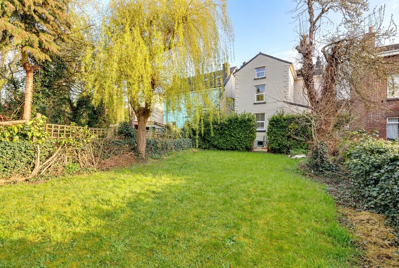 Large garden with lawn, mature trees, and adjacent residential properties visible