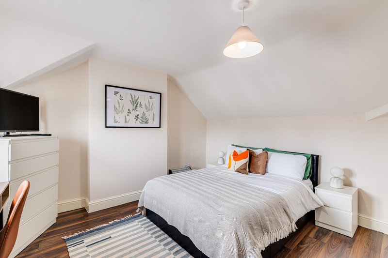 Bright attic bedroom with double bed, white nightstand, pendant light and framed wall art