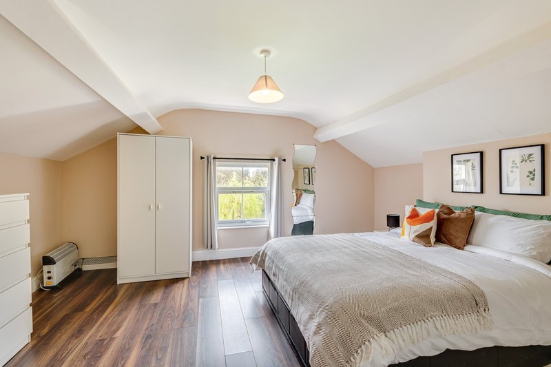 Bright attic bedroom with double bed, white wardrobe, wooden floor and window