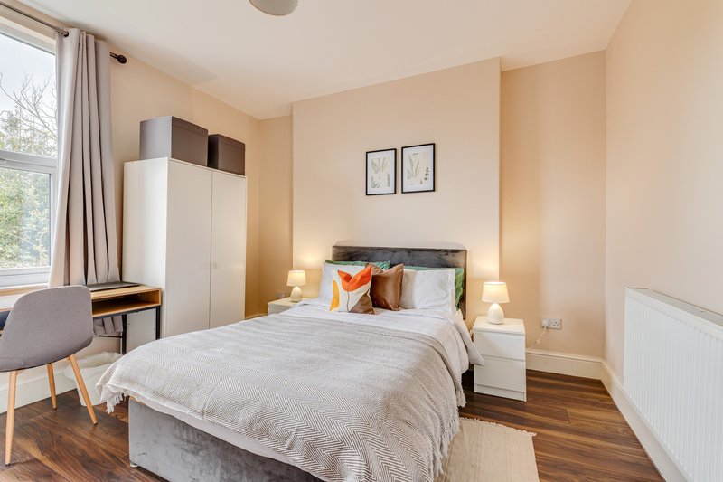 Bright bedroom with double bed, wooden floor, wardrobe, desk and window with curtains