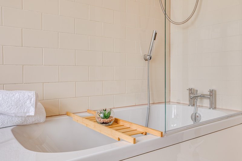 Modern bathroom with white subway tiles, soaking tub, wooden bath caddy, and white towels