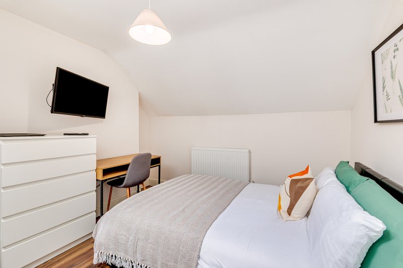 Bright bedroom with double bed, white dresser, desk, wall-mounted TV and pendant light
