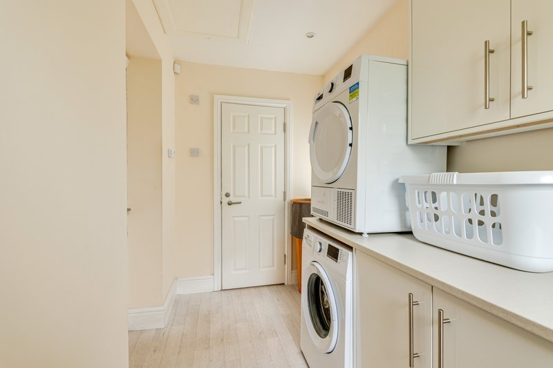 Laundry room with stacked washing machines, white cabinetry, and cream-colored walls