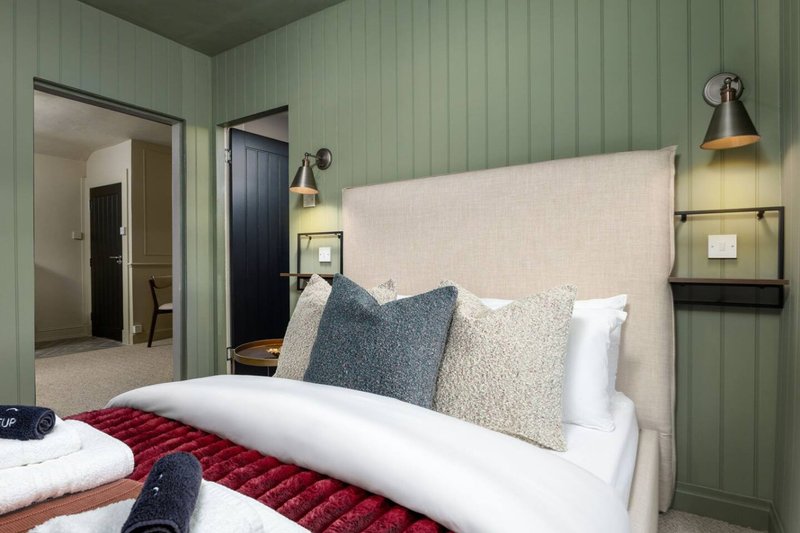 Modern bedroom with cream headboard, grey and white pillows, red throw, green paneled walls and pendant lighting