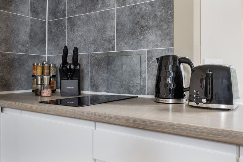 Modern kitchen counter with black appliances, knife block, kettle and toaster against grey tile backsplash