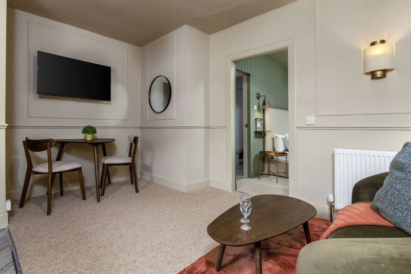 Modern hotel room with dining area, TV, sofa, and ensuite bathroom visible