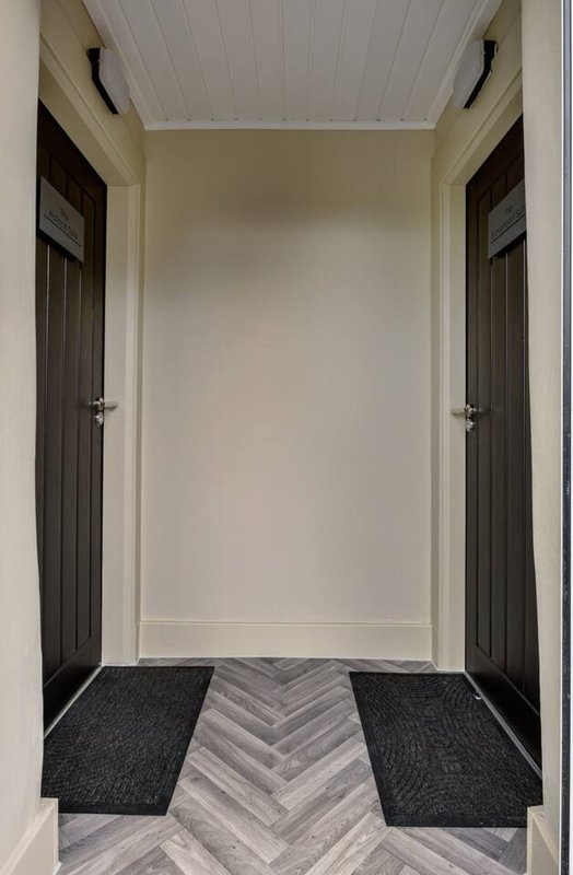 Modern hallway with white ceiling, dark doors, herringbone flooring and black entrance mats