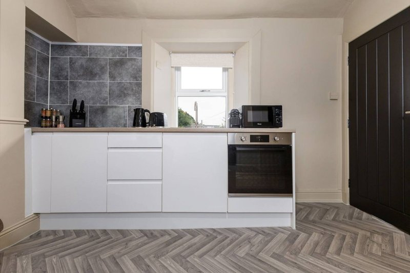 Modern kitchen with white cabinetry, dark tile backsplash, integrated oven, and herringbone flooring