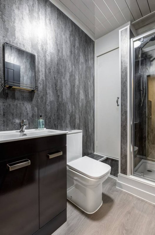 Modern bathroom with dark vanity, grey textured wall, toilet, and walk-in shower enclosure