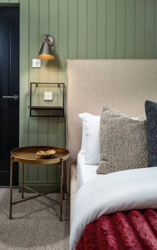 Modern bedroom with upholstered headboard, white bedding, textured cushions, wooden side table with lamp