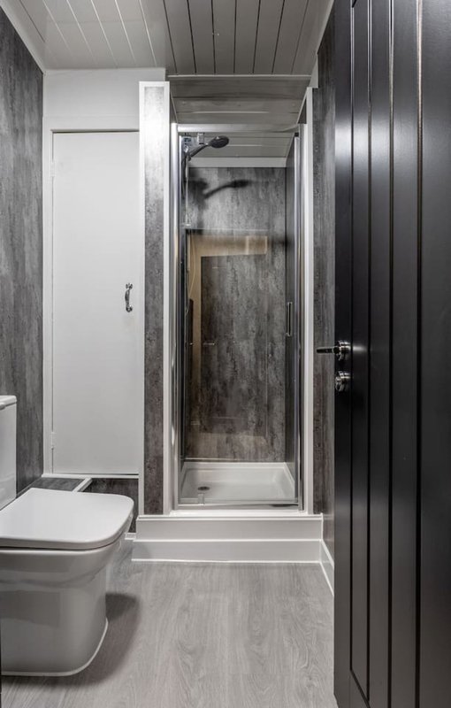 Modern bathroom with toilet, shower enclosure, grey tile walls and wood-effect flooring