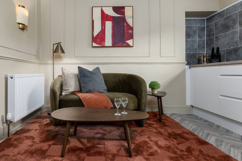 Modern living room with olive green sofa, mid-century coffee table, red rug and wall art