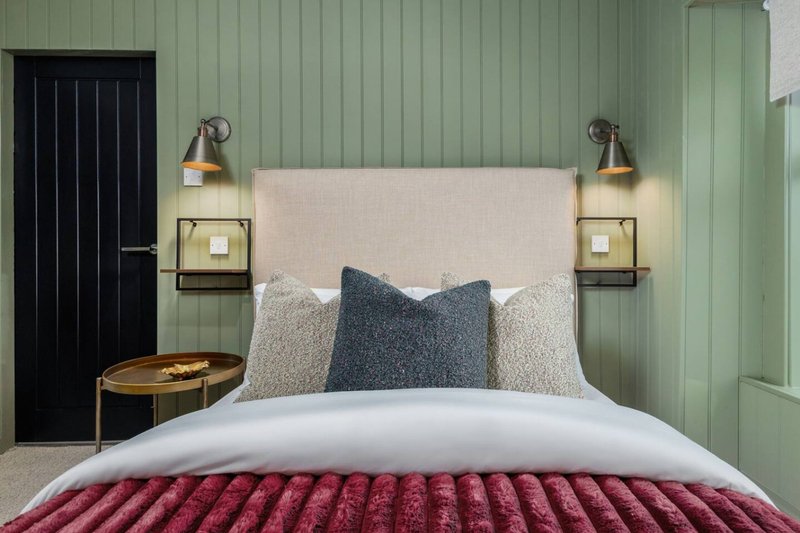 Modern bedroom with cream headboard, burgundy bed runner, patterned pillows and sage green walls