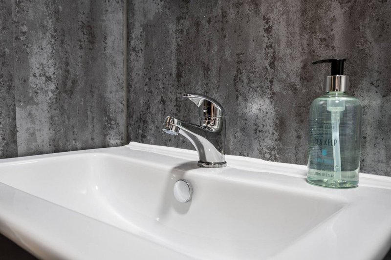 Modern bathroom sink with chrome tap and hand soap dispenser against grey tile wall