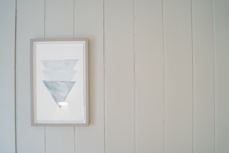 White shiplap wall with framed geometric triangle artwork in gray frame