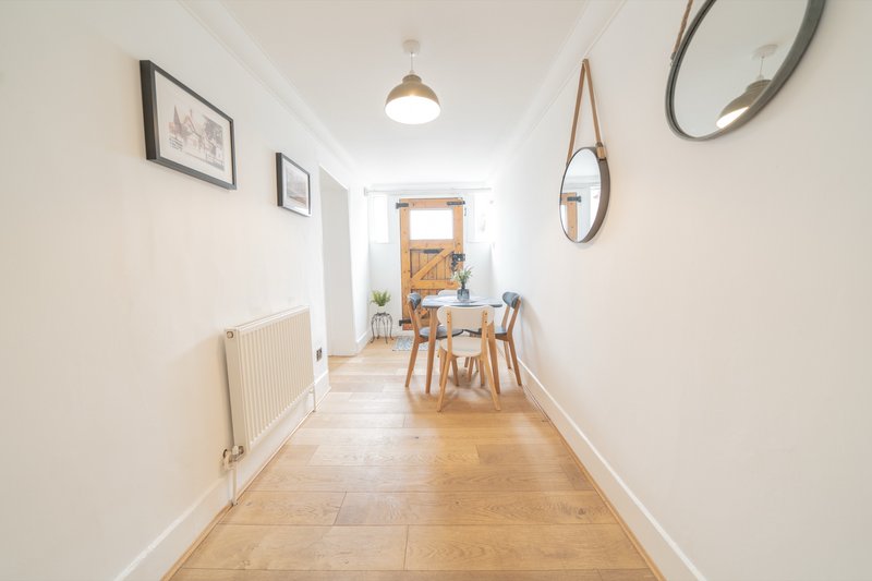 Bright hallway with wooden floor, white walls, framed artwork, pendant light and dining area visible