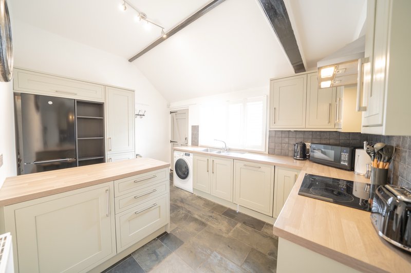 Modern kitchen with cream cabinetry, wood countertops, built-in appliances and skylight