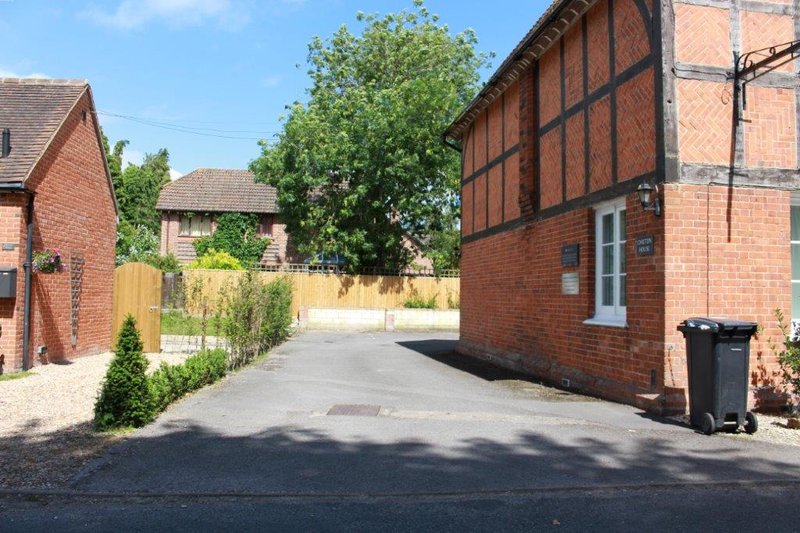 Brick cottage exterior with driveway, garden fence, and trees on sunny day