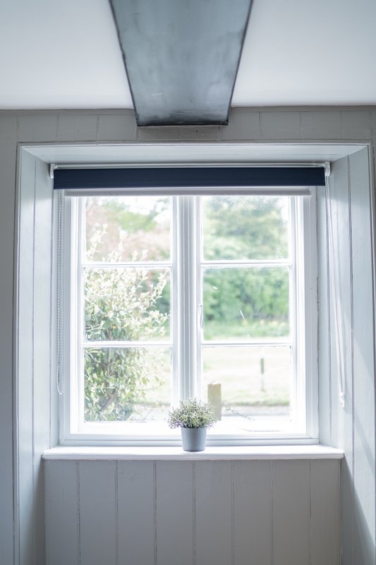 Bright interior window with white frame, dark roller blind, and small potted plant on sill