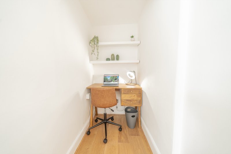 Narrow home office with wooden desk, chair, shelving, small plants and desk accessories